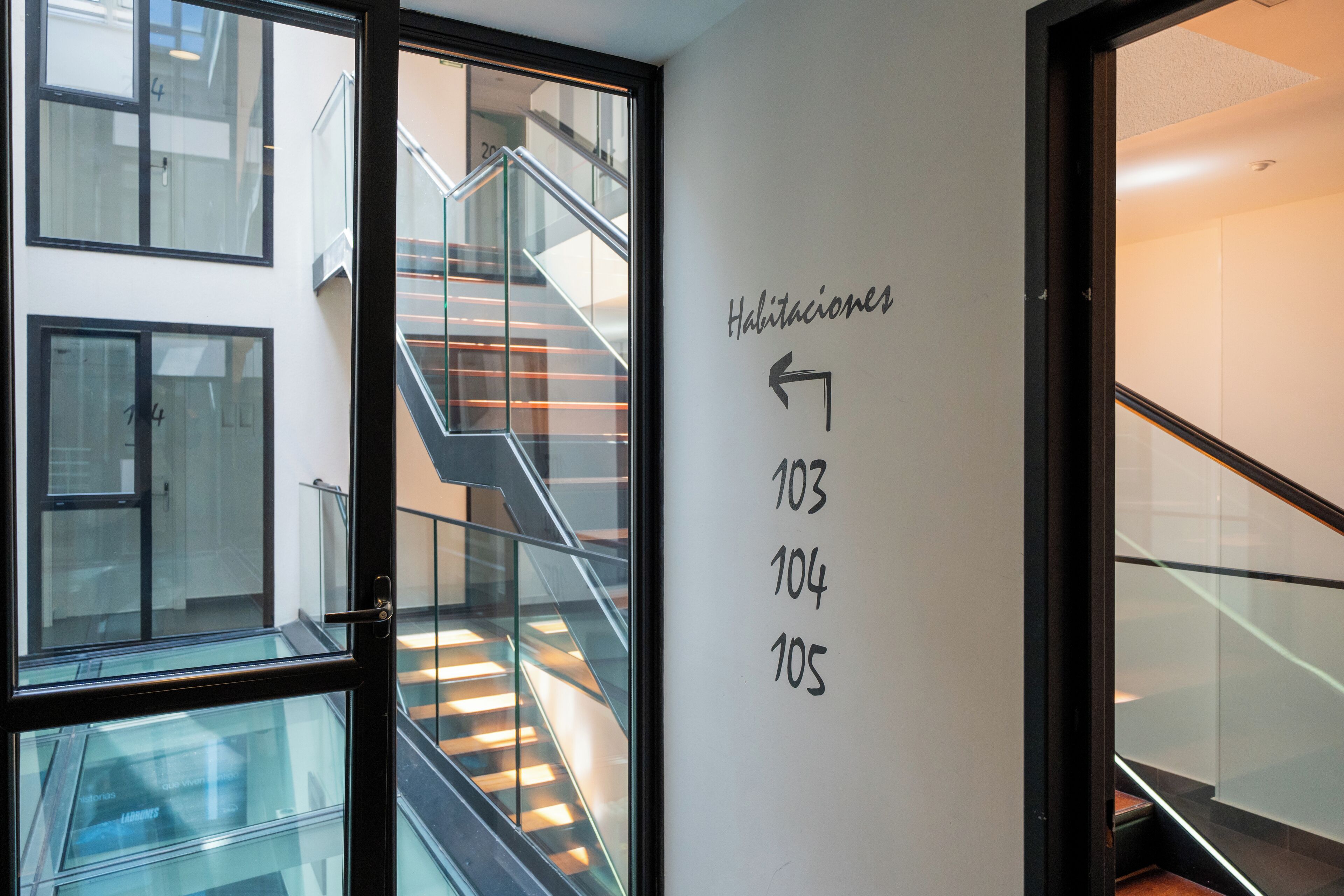 Een modern interieur met een trap, glazen hekwerk en een muur met de nummers 103, 104 en 105.