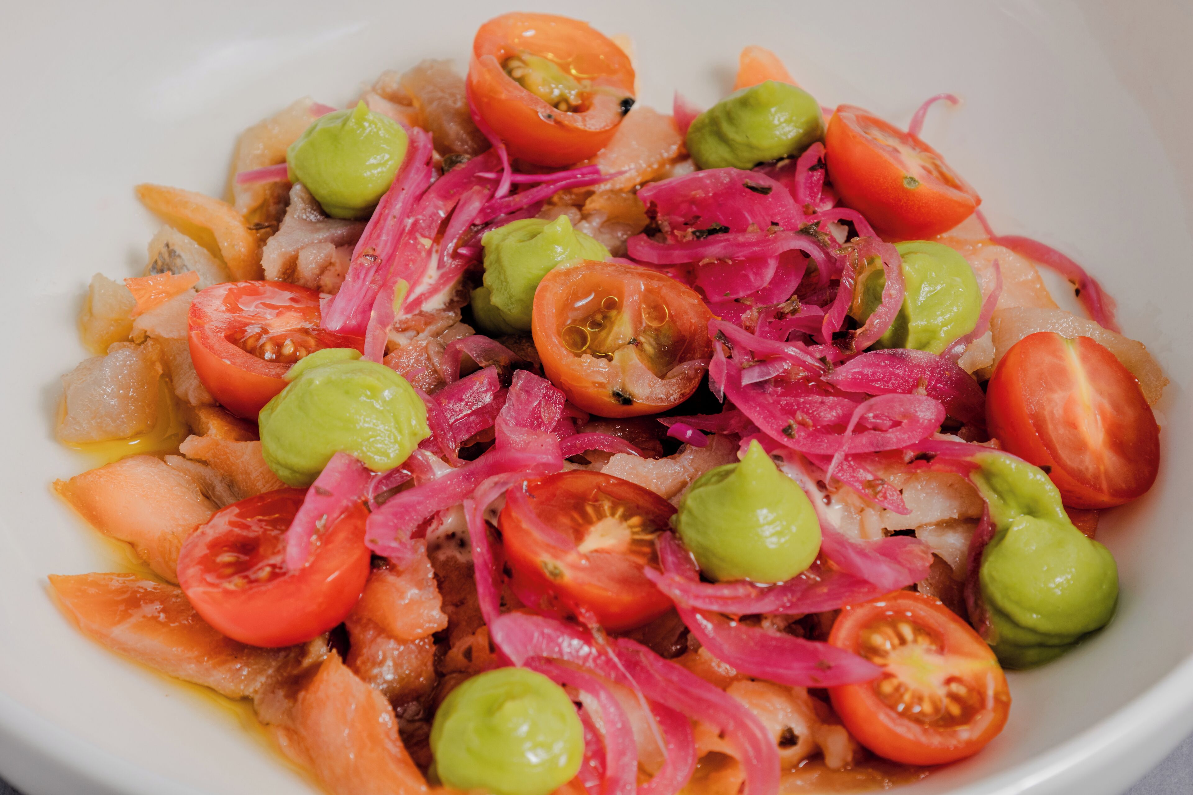 A bowl of salad with tomatoes, onions, and avocado.