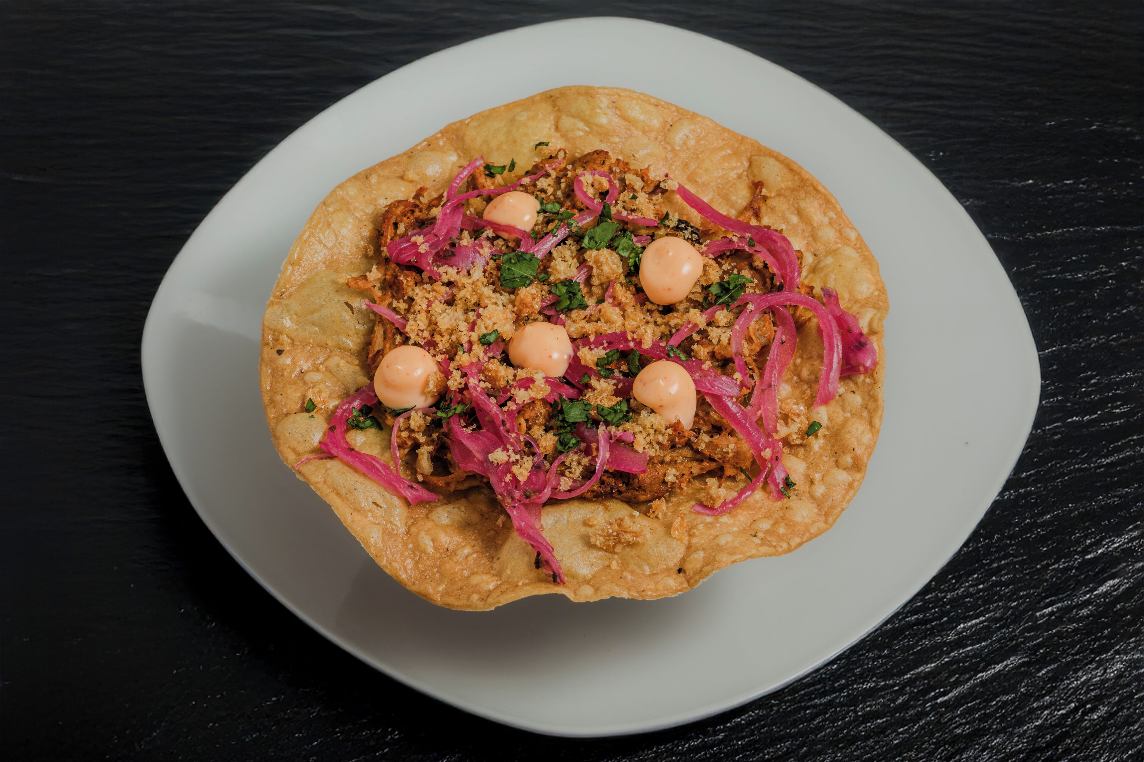 A plate with a stuffed flatbread topped with red onions, herbs, and two boiled eggs.