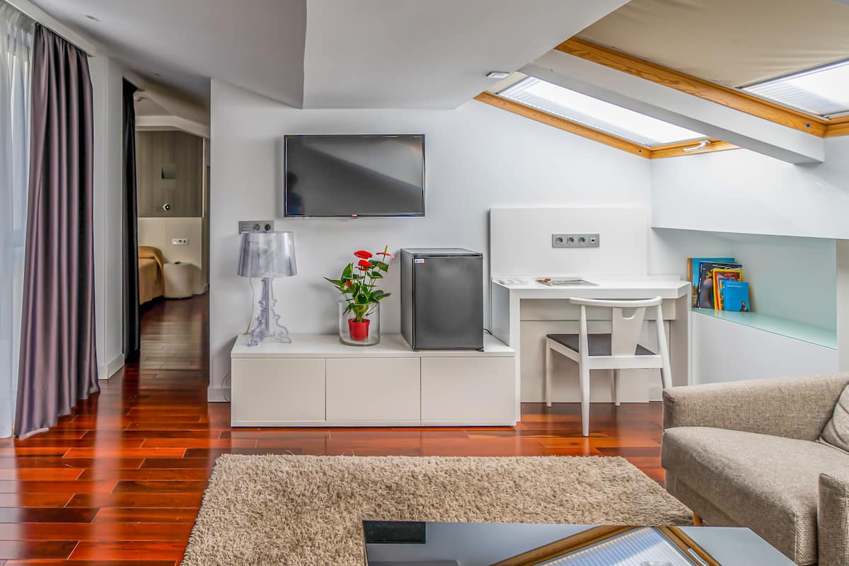 A modern living room with a flat-screen TV, a small refrigerator, a white desk, and a comfortable sofa.