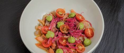 Un tazón blanco con una ensalada de tomates, cebollas y aceitunas verdes sobre una superficie oscura.