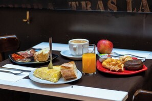 Una mesa de desayuno con platos de comida, una taza de café, un vaso de jugo de naranja y un croissant.