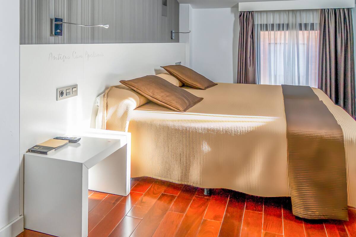 A modern hotel room with a bed, a desk, and a large window with curtains.