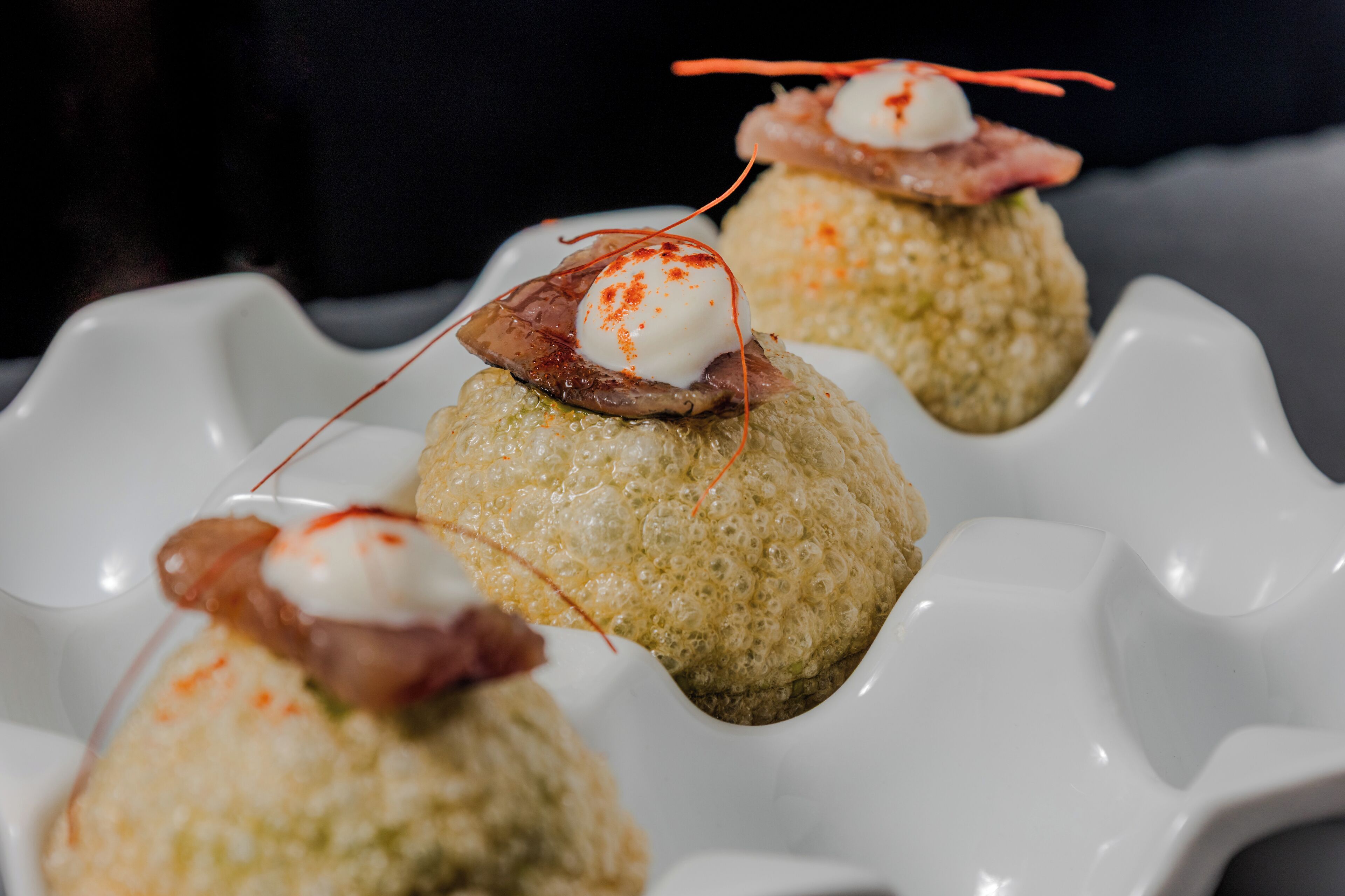 Tres alimentos redondos y con textura sobre un plato blanco con borde festoneado.