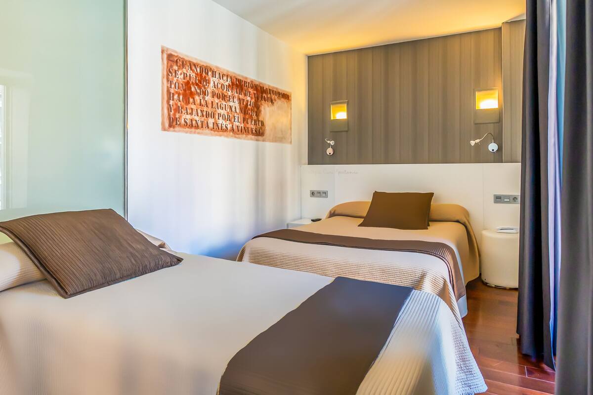 A hotel room with two beds, a wall-mounted artwork, and bedside lamps.