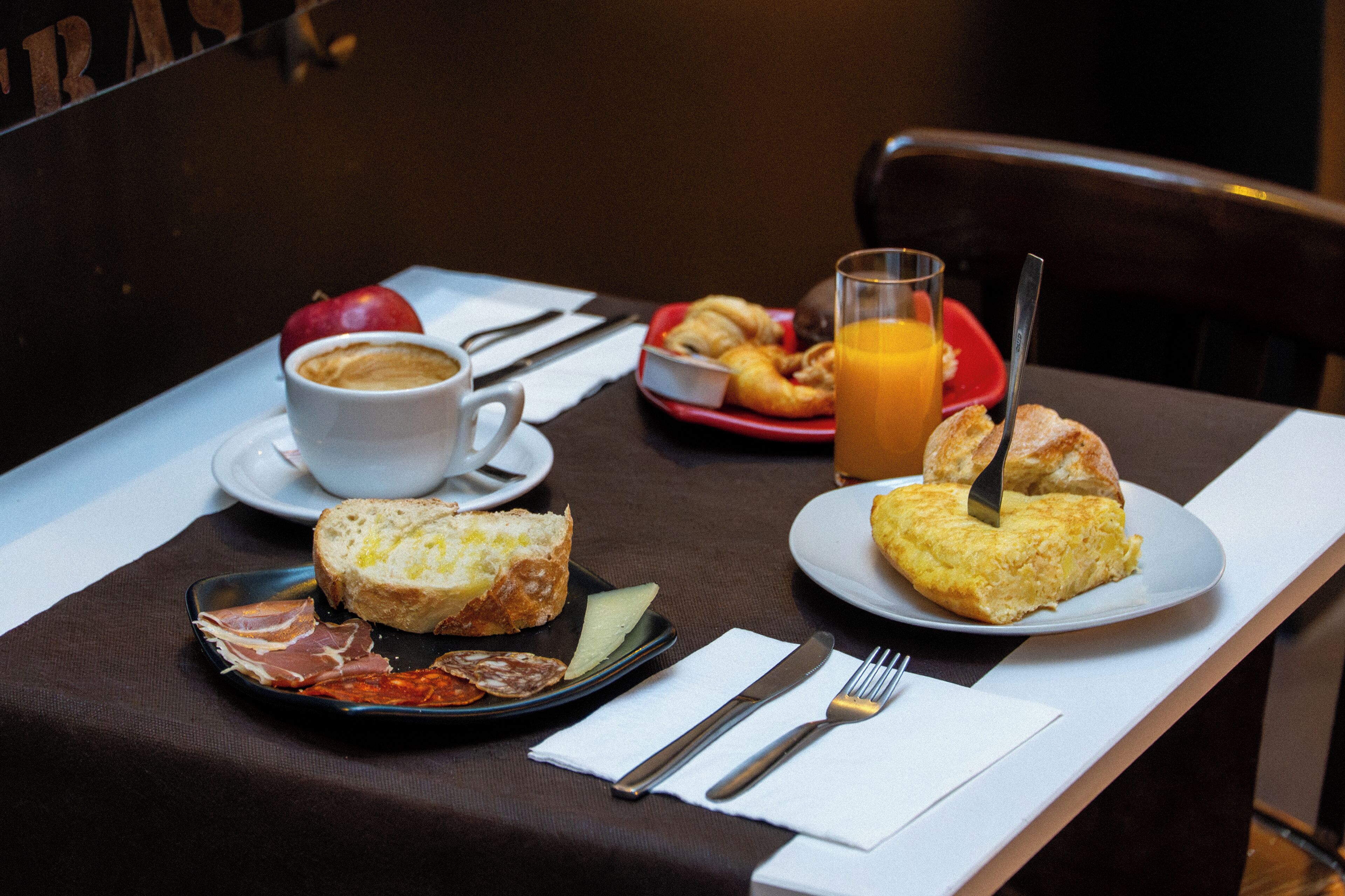 A breakfast setting with croissants, a plate of ham, a cup of coffee, and a glass of orange juice on a table.