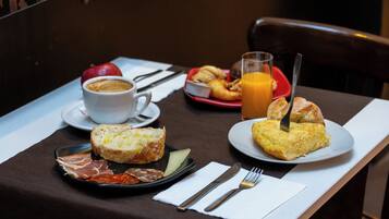 A breakfast setting with croissants, a plate of ham, a cup of coffee, and a glass of orange juice on a table.