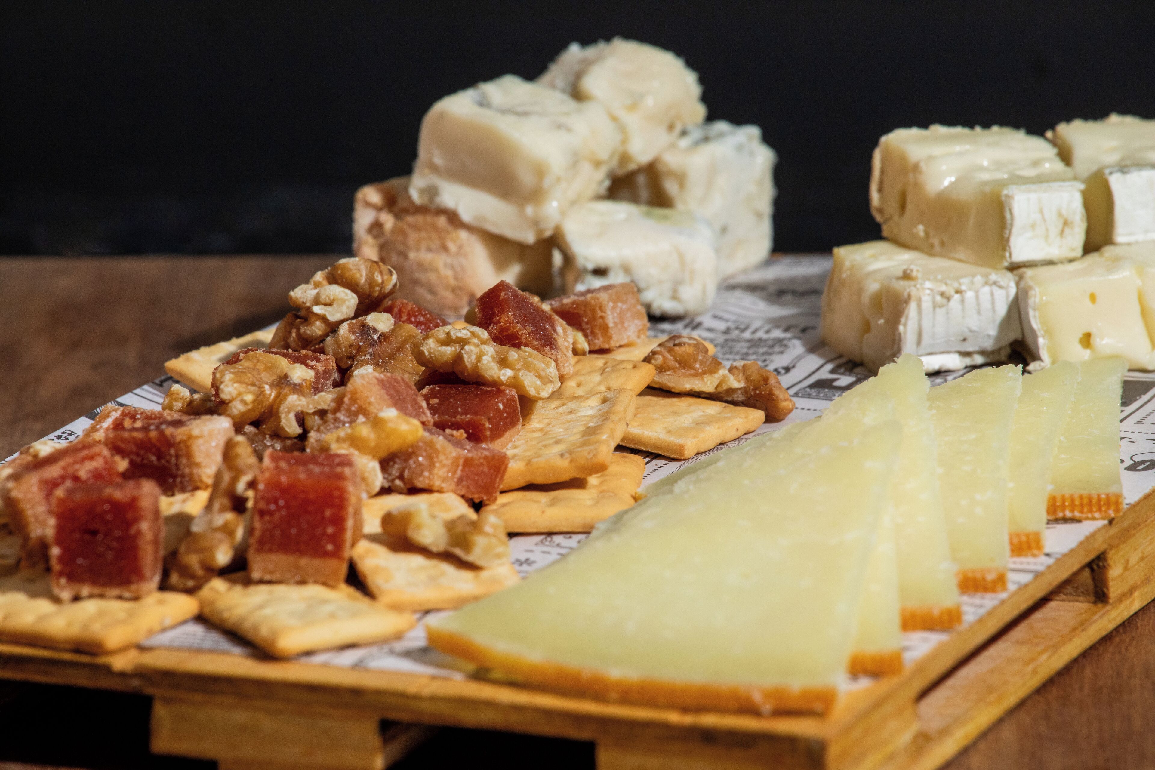 A wooden board with various cheeses, crackers, and nuts.