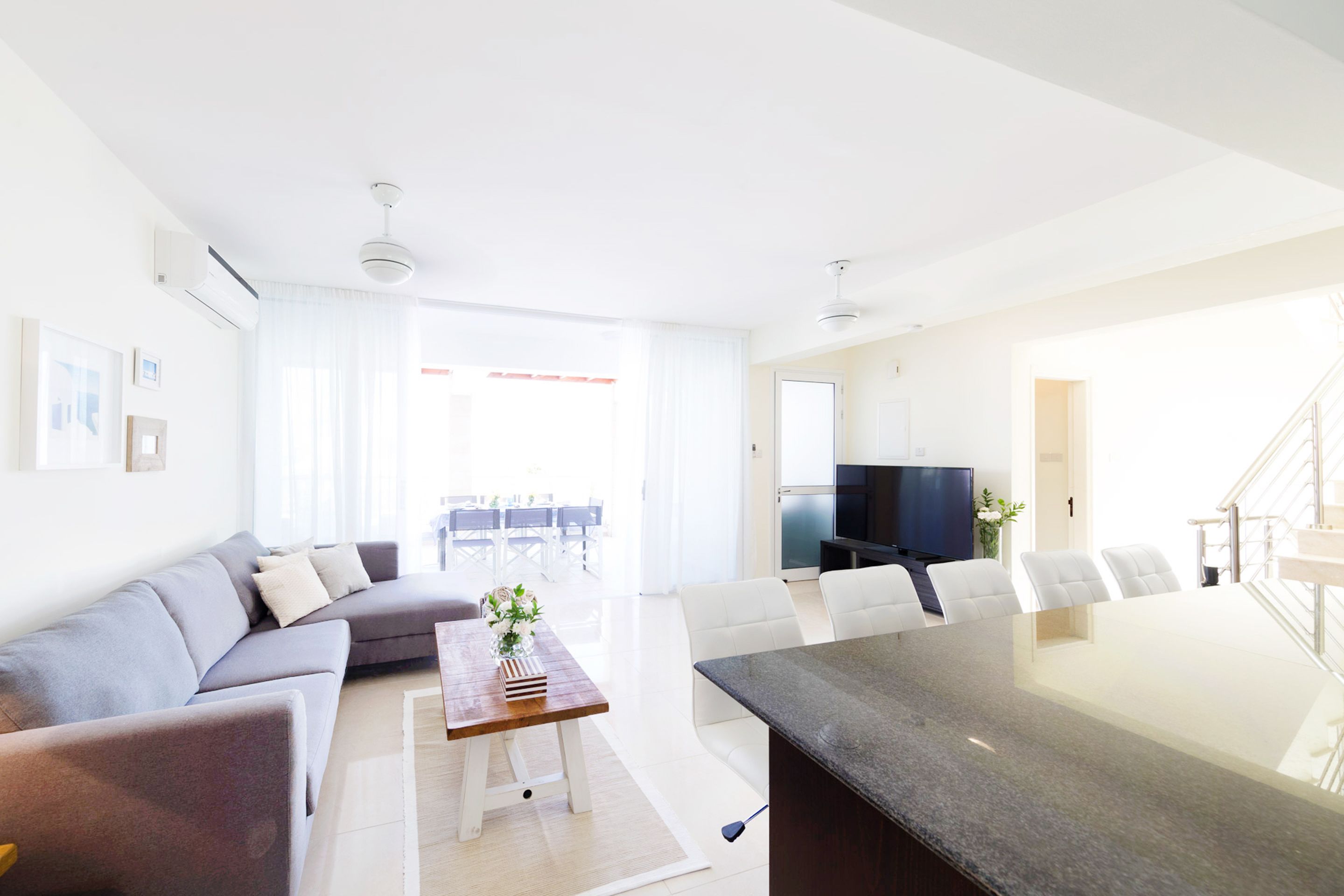 A modern living room with a grey sofa, white chairs, a wooden coffee table, and a large TV.