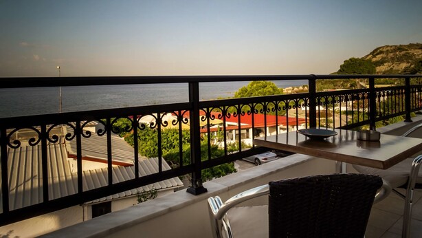 A balcony with a view of the sea, a dining table, and a wicker chair. - Tsambikos Apts (Rhodes)