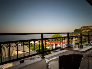 A balcony with a view of the sea, a dining table, and a wicker chair. - Tsambikos Apts (Rhodes)