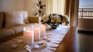 A cozy room with a sofa, a table with candles, a vase of flowers, and a plant. - Tsambikos Apts (Rhodes)