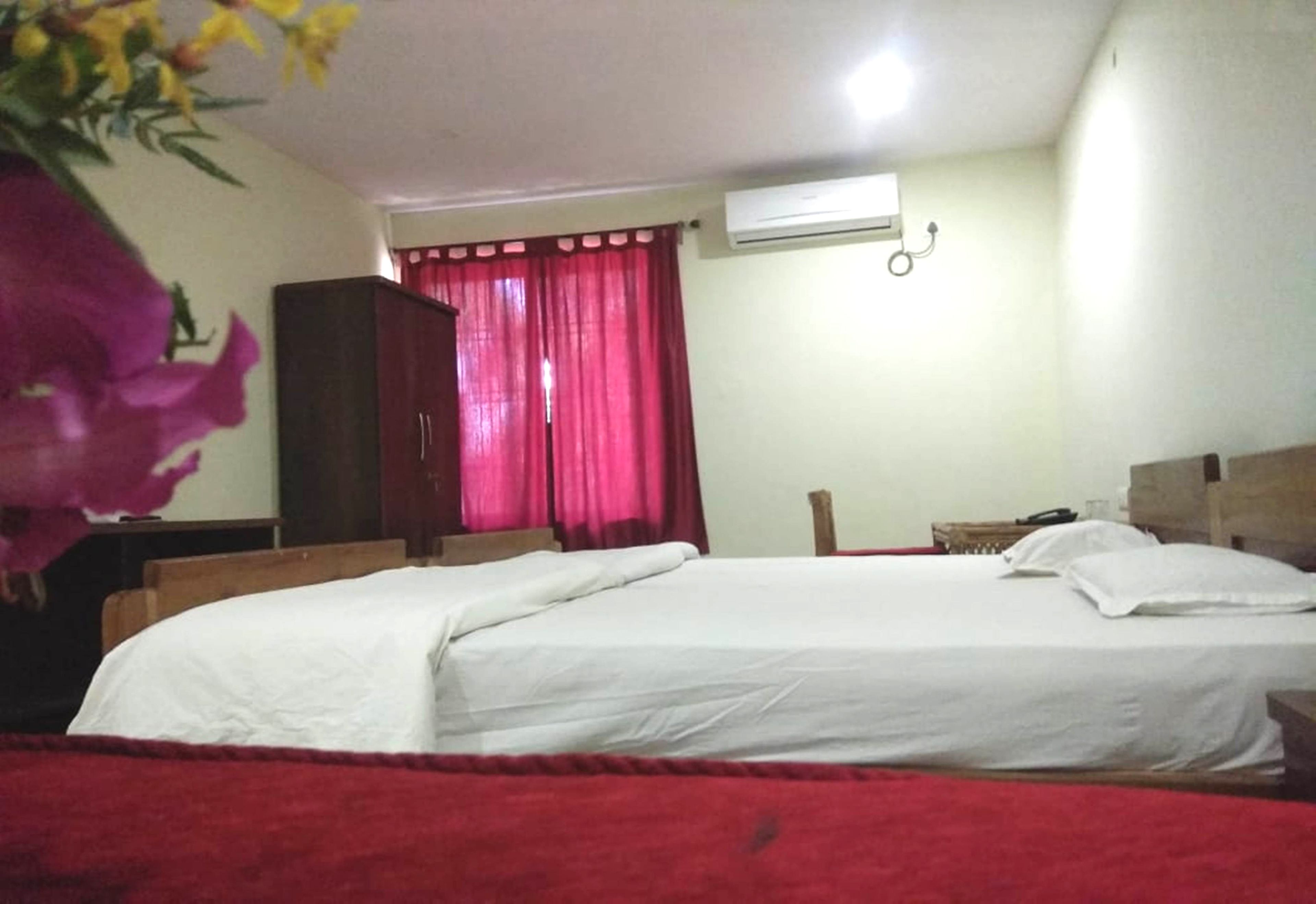 Un dormitorio con cama, armario, mesita de noche y ventana con cortinas rojas.