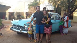 Una familia posando frente a un coche antiguo con un edificio al fondo.