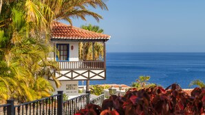 Un edificio frente al mar con un balcón y abundante vegetación.