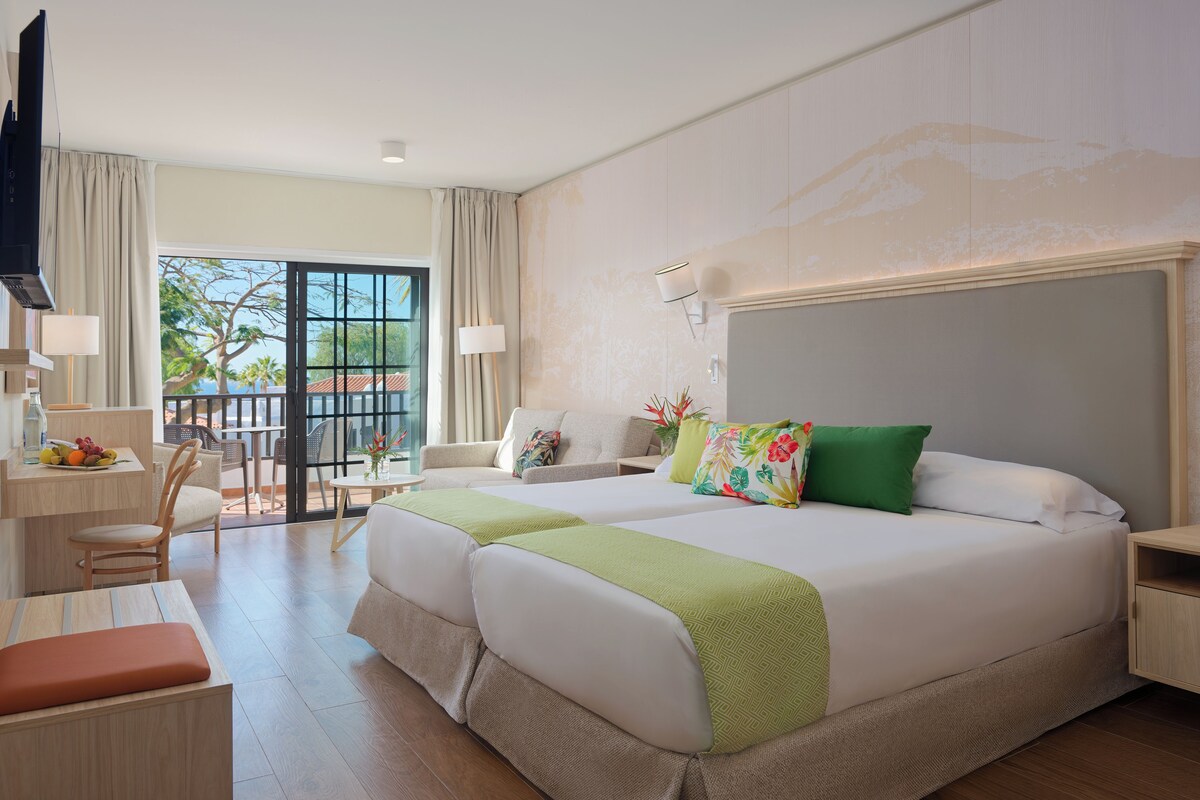 A hotel room with a large bed, a desk, a chair, and a view of the outdoors.