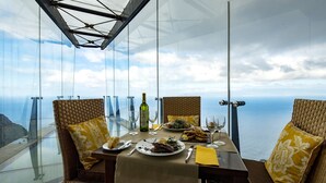Mesa para dos con vista al océano, una botella de vino y platos de comida.