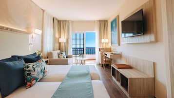Een hotelkamer met een bed, een bank, een bureau, een televisie en een balkon met uitzicht.
