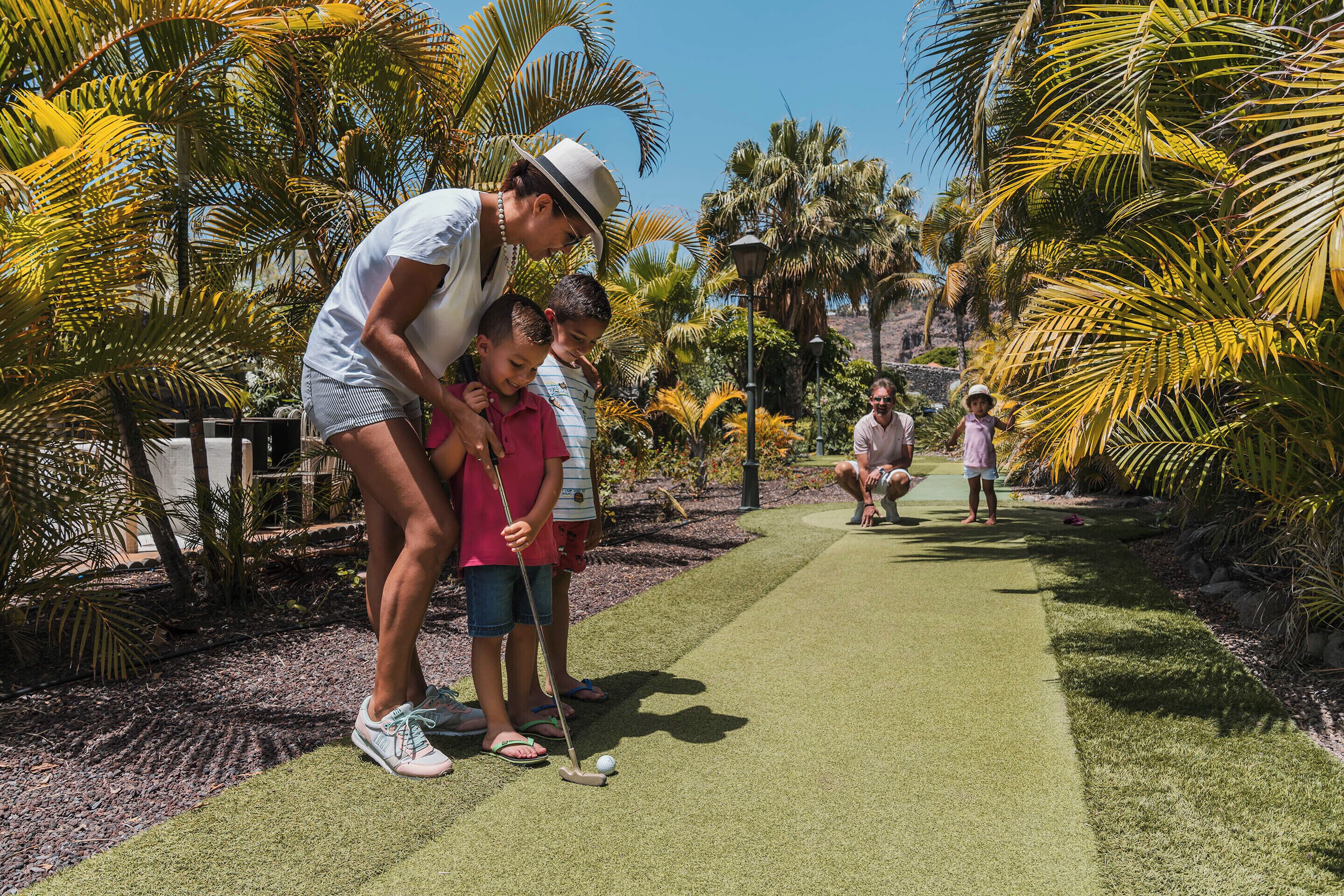 Een golfbaan met een putting green, palmbomen en een heldere lucht.