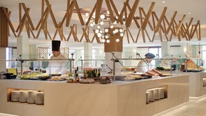Montaje moderno de bufé con un chef preparando comida, una vitrina de vidrio y una estructura decorativa en el techo.
