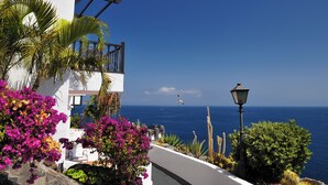 Un edificio frente al mar con balcones, rodeado de buganvillas y cactus.