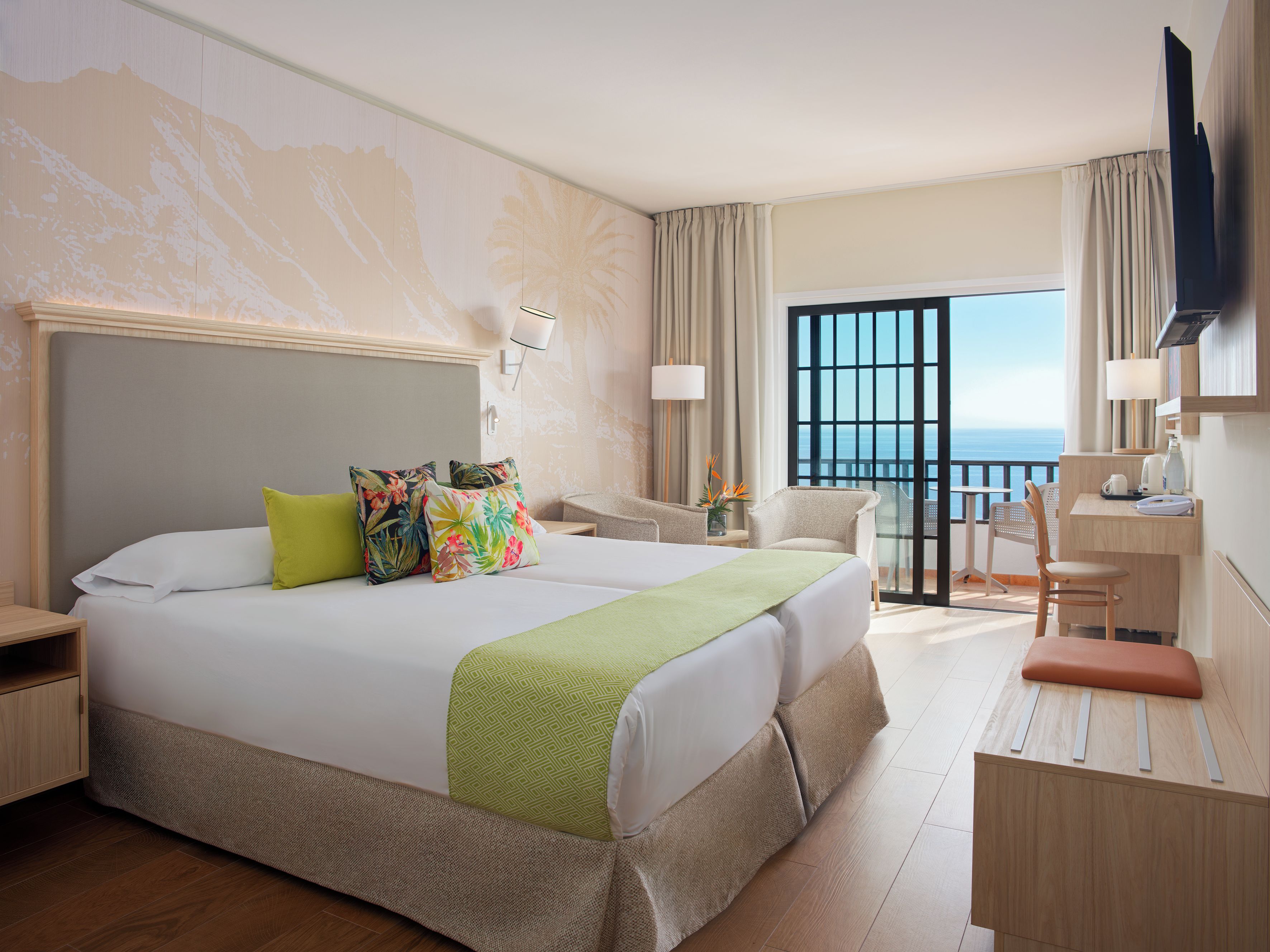Habitación de hotel con una cama grande, un escritorio, una silla, un televisor y un balcón con vista al mar.