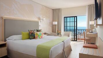 Habitación de hotel con una cama grande, un escritorio, una silla, un televisor y un balcón con vista al mar.