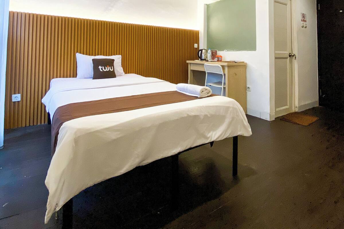 A hotel room with a bed, a desk with a chair, a mirror, and a door.