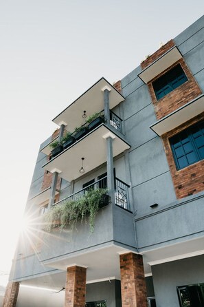 A multi-story building with a modern architectural design, featuring balconies with plants, large windows, and a prominent brick column. - Tuju Abuserin Syariah (Jakarta)