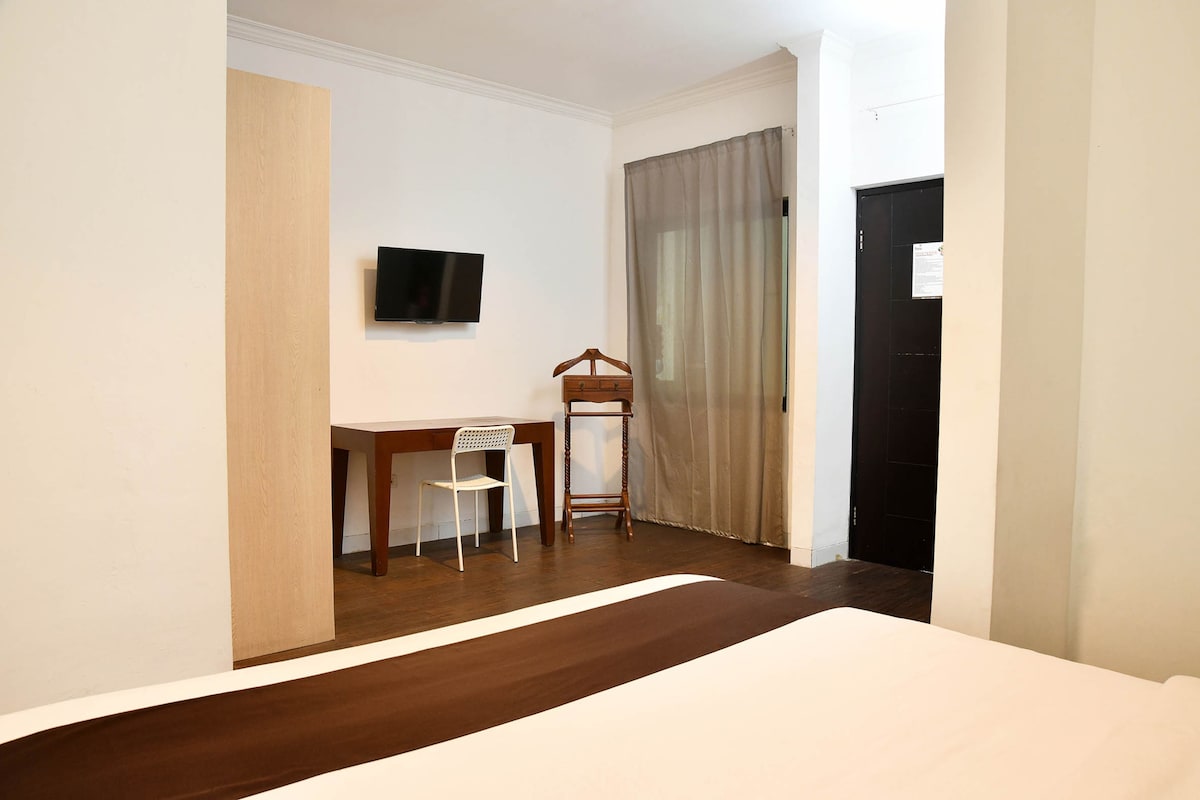 Ein Hotelzimmer mit Bett, Schreibtisch, Stuhl, Fernseher und Kleiderschrank.