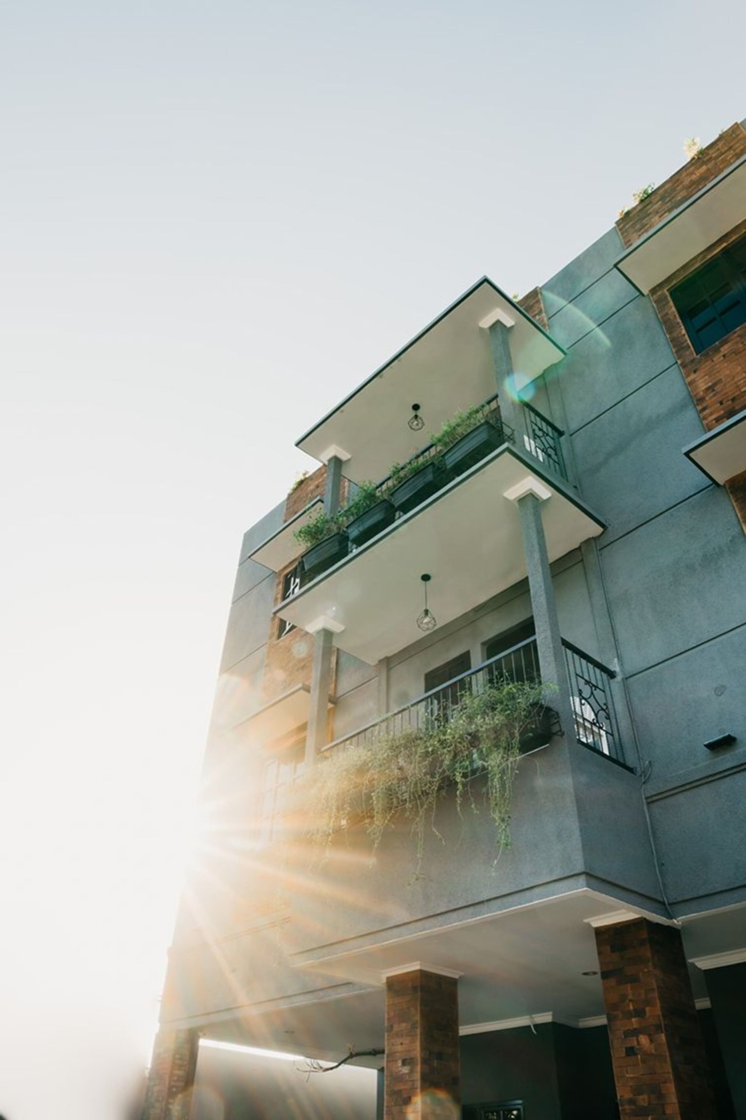 A multi-story building with a balcony on the second floor, featuring a small garden area.