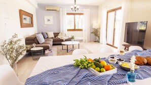 A modern living room with a sofa, coffee table, and a dining area with a fruit basket and tableware. - Villa Mojito (Pegeia)