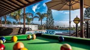 A pool table with balls, a pool, and a view of palm trees and a clear sky. - Villa Mojito (Pegeia)