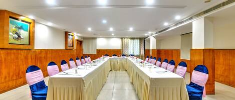 A conference room with a long table, chairs with pink and blue sashes, wooden paneling, and ceiling lights.