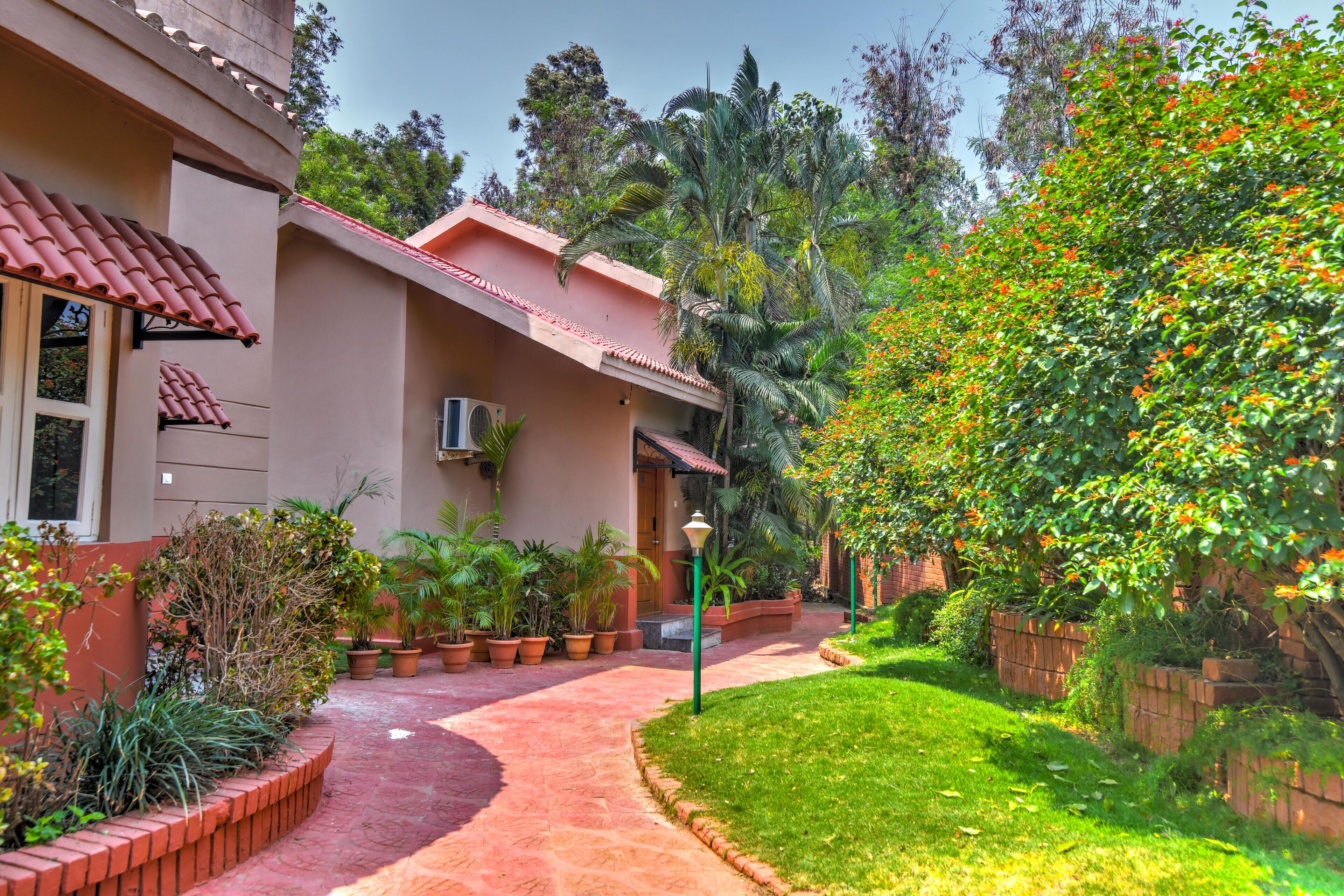 A pathway leading to a building with a red-tiled roof, surrounded by potted plants and a well-maintained lawn.