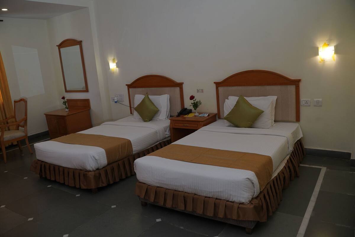 A hotel room with two beds, a desk, a chair, and a mirror.