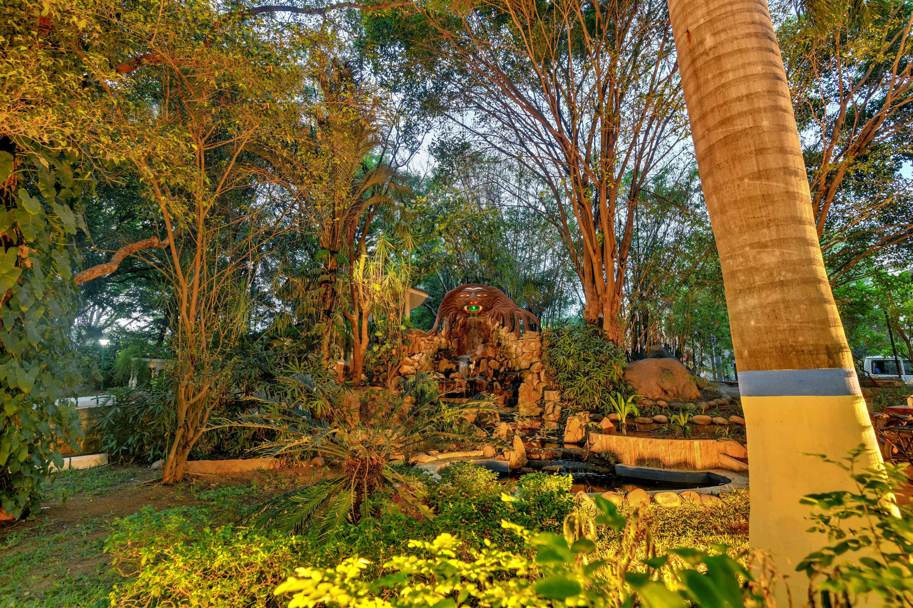 A lush garden with a variety of trees, a small waterfall, and a stone structure.