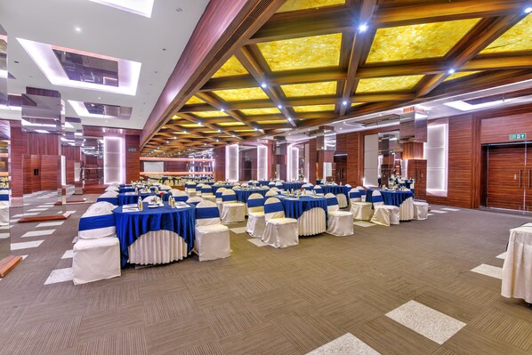 Un amplio salón de banquetes con filas de mesas dispuestas para eventos, que presenta un diseño moderno de techo y paneles de madera.