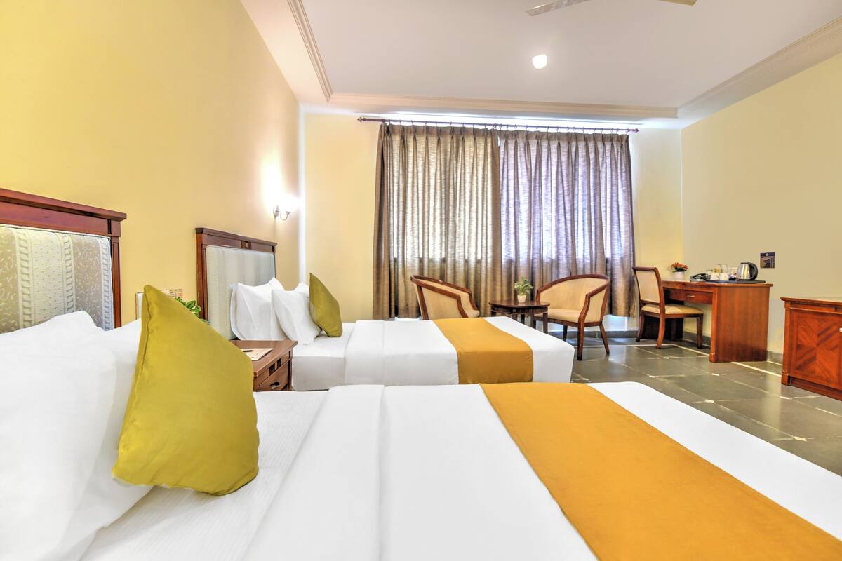 A hotel room with two beds, a desk, a chair, and a large window with curtains.