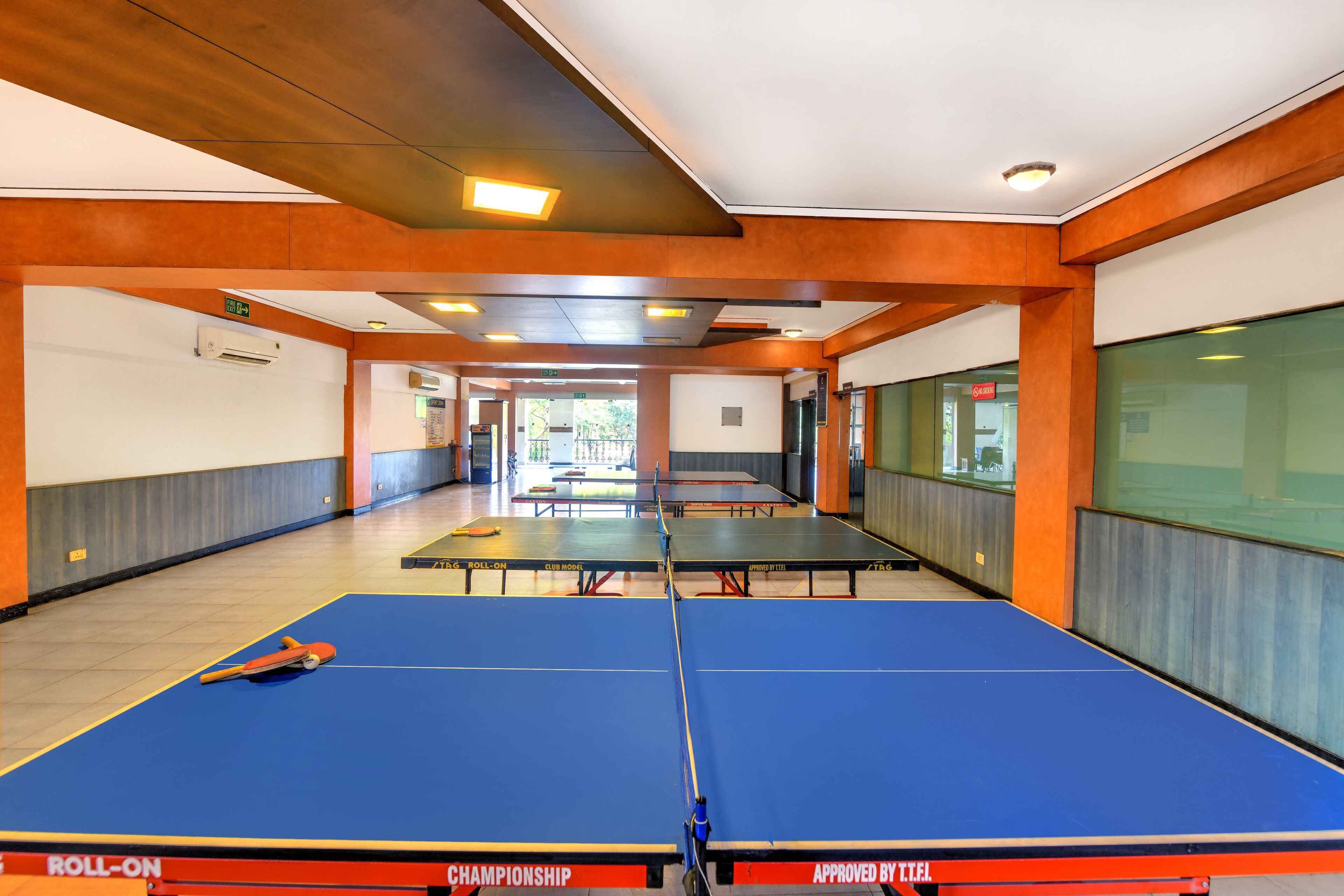 Un espacio interior amplio con varias mesas de ping pong, vigas de madera en el techo y un ambiente luminoso y bien iluminado.