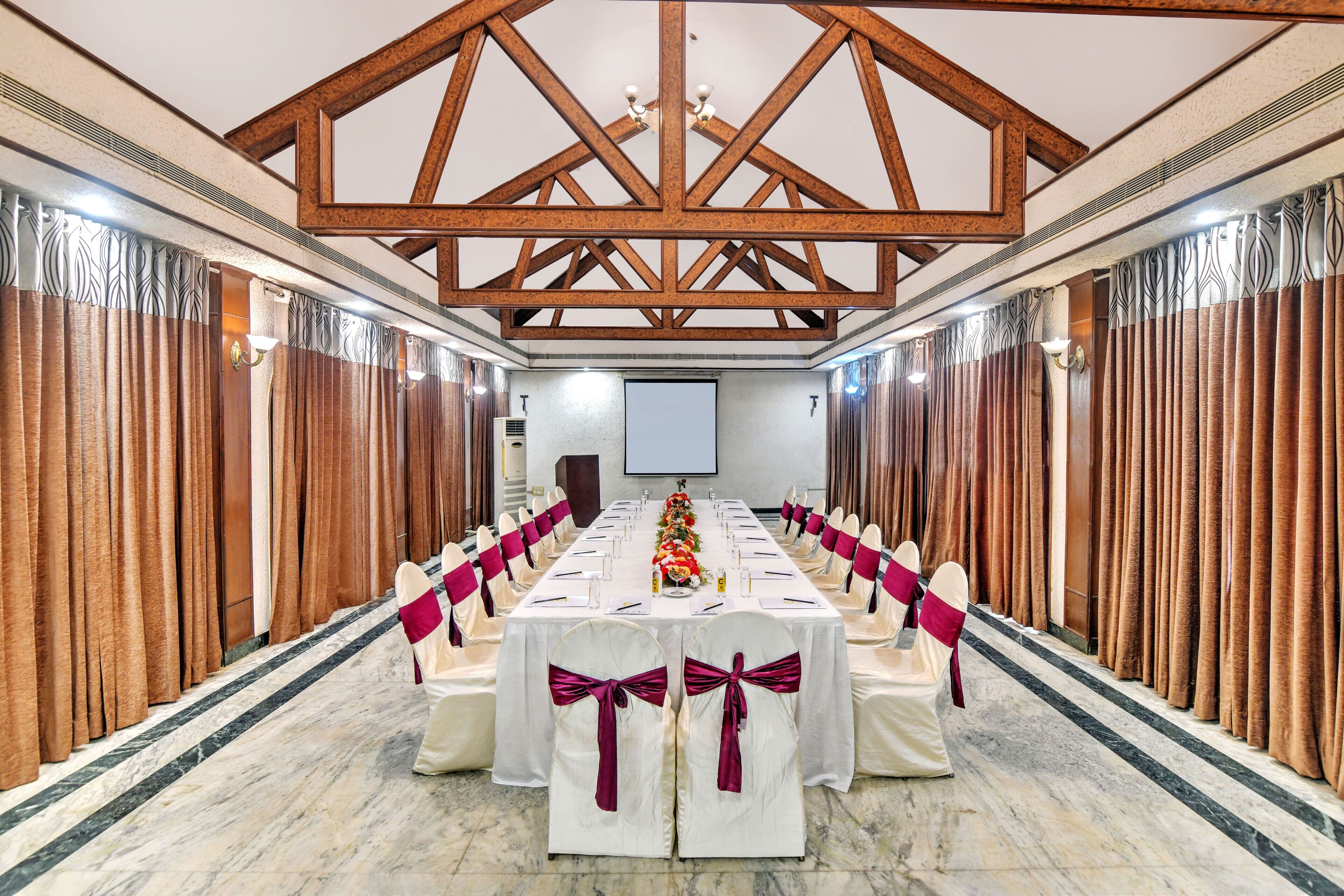 A conference room with a long table, white chairs with red sashes, wooden beams on the ceiling, and curtains on the walls.