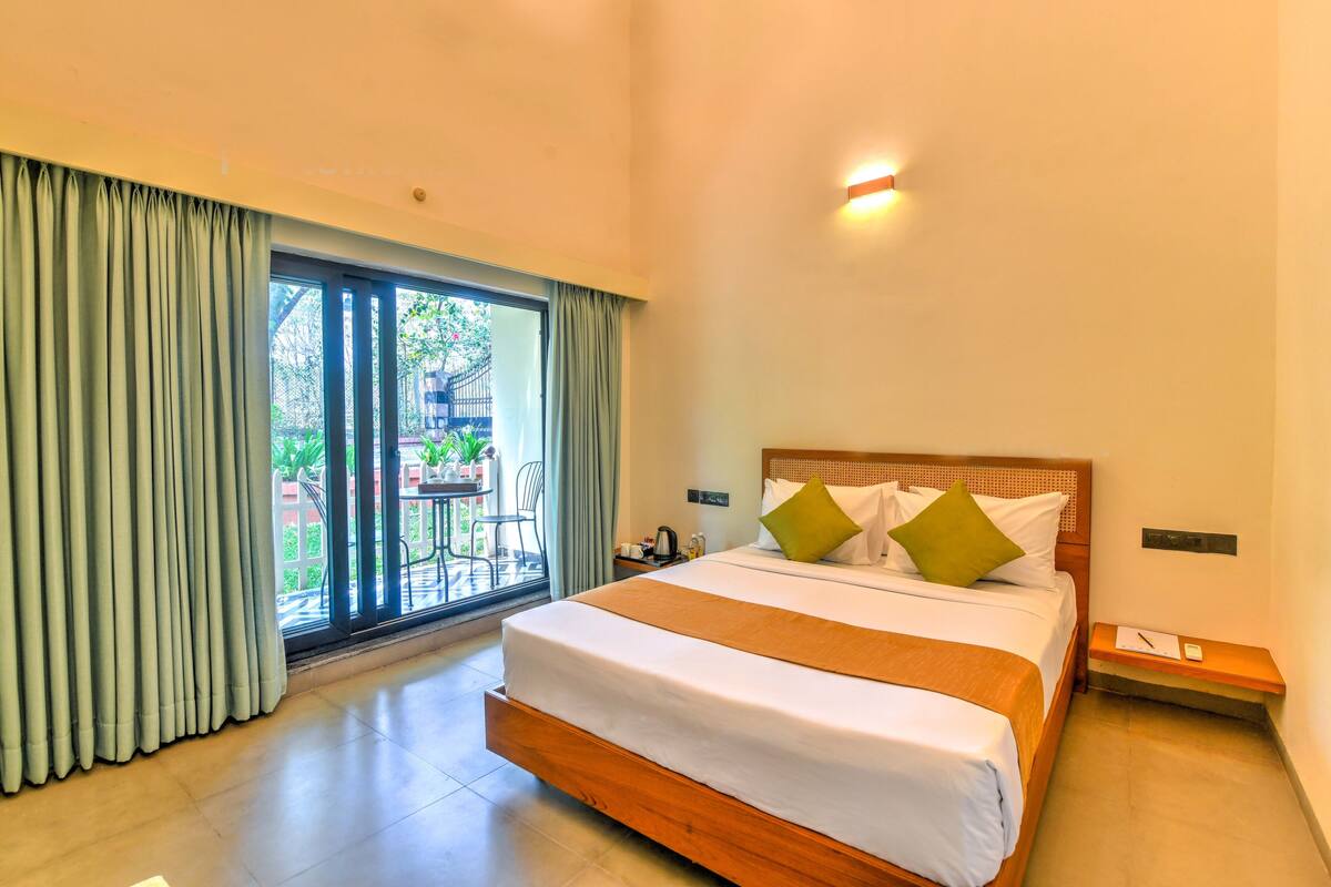 A hotel room with a large bed, a nightstand, a window with curtains, and a view of the outside.