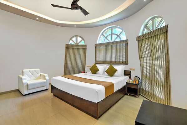 A modern hotel room with a large bed, a white armchair, and a ceiling fan.