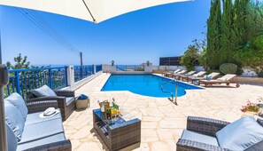 A rooftop pool area with lounge chairs, a table with drinks, and a view of the sea. - Villa Neptune (Pegeia)