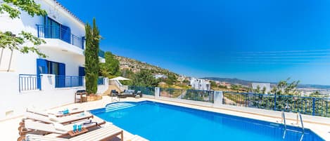 A poolside area with a clear view of the sea and a hillside in the background.
