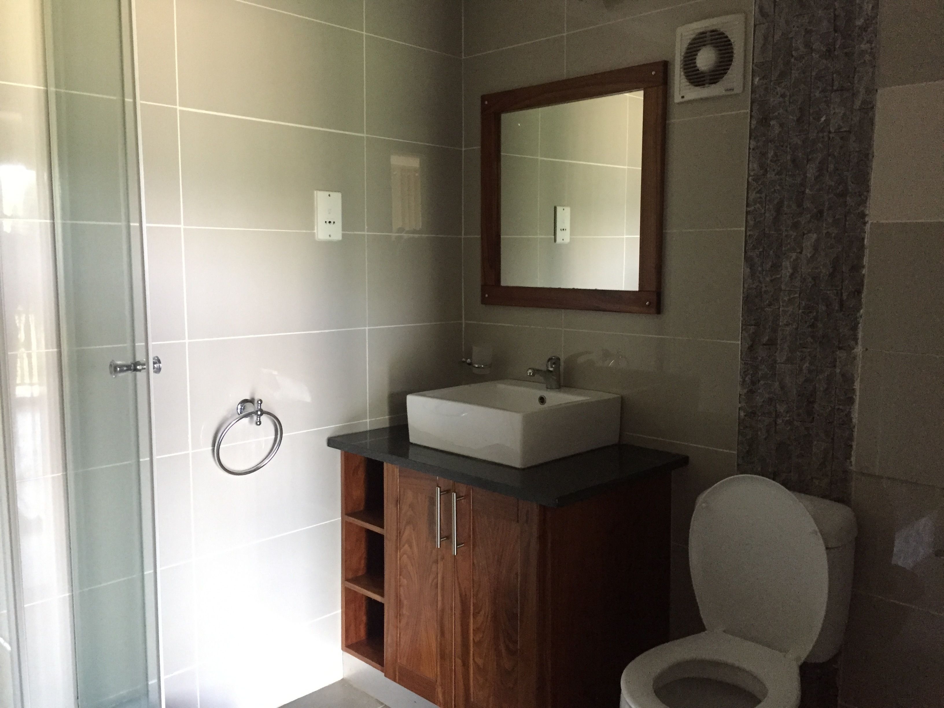 Une salle de bain avec une douche à parois de verre, un meuble-lavabo en bois et des toilettes.