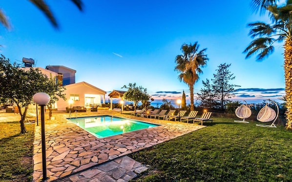 A pool area with lounge chairs, a stone pathway, and a building with a sloped roof.