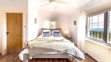 Une chambre à coucher avec un lit, un ventilateur de plafond, une fenêtre donnant sur un beau paysage et une porte en bois.