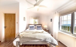 A bedroom with a bed, a ceiling fan, a window with a view, and a wooden door.