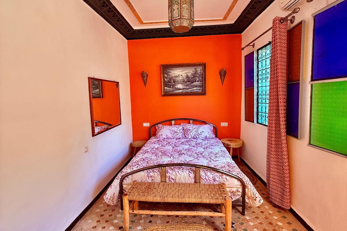 A room with a bed, a woven mat, a painting, and a patterned ceiling.